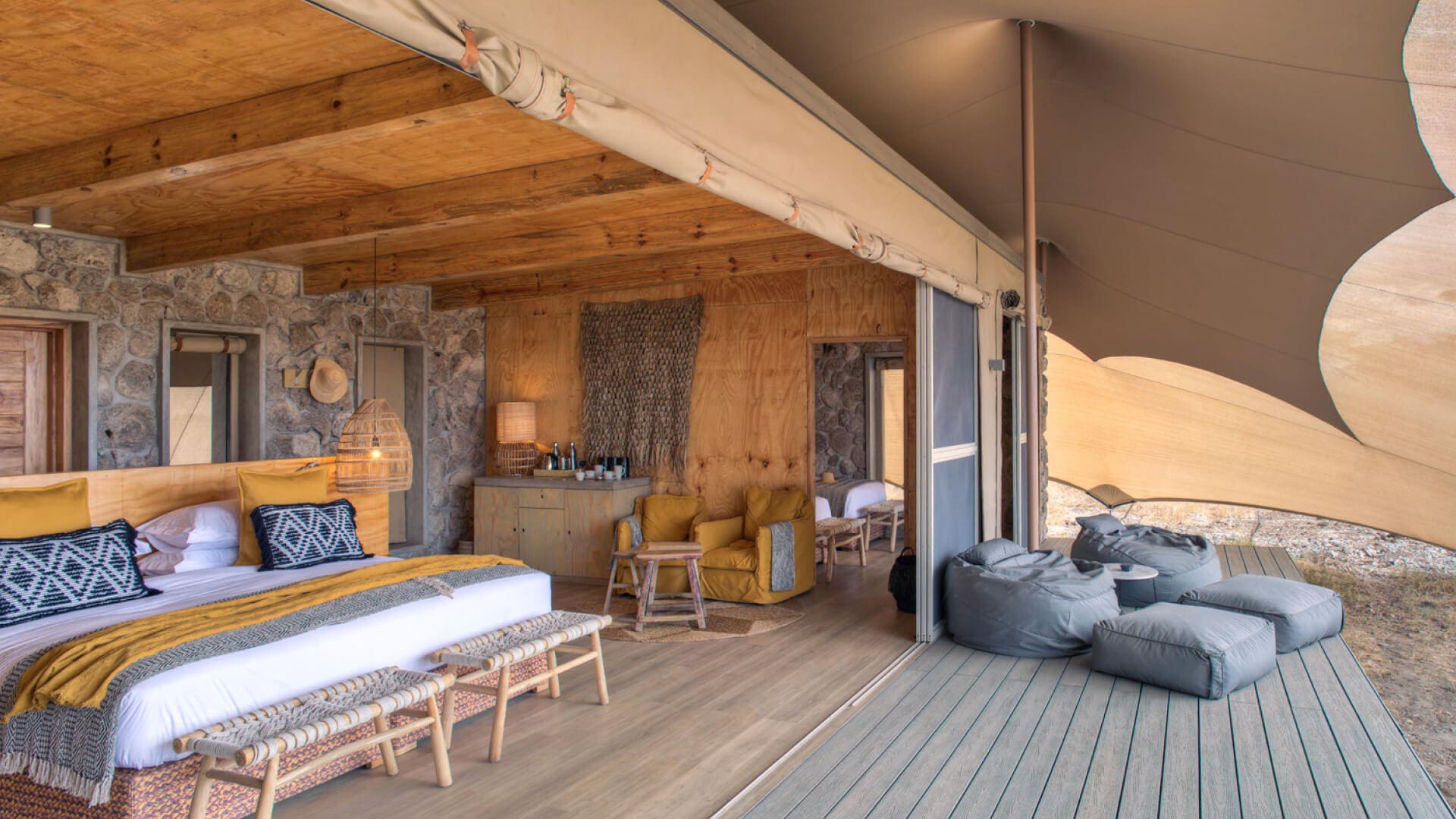 Namiri Plains, Serengeti National Park, view of the interior, double guest tent, bed with pillows and throw blanket, hanging lights, lamp on the side table with coffee station, bean bags on the deck, doors open
